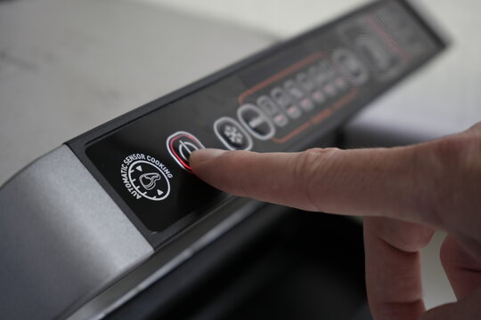 A man's finger presses the power button on a home electric grill to turn it off. Household electrical appliances in the home kitchen. Black electric grill control panel close-up.