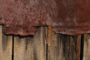 A wooden fence aging over the years with a sheet of old iron nailed to it for reinforcement is...