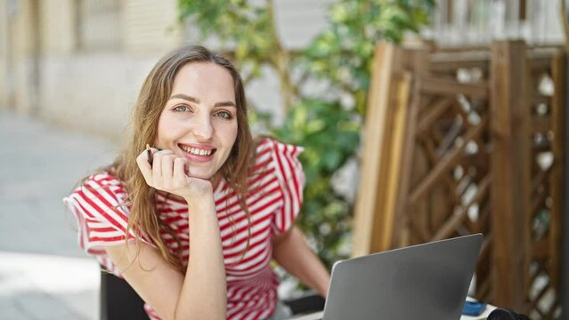 Young blonde woman using laptop sitting on table at coffee shop terrace