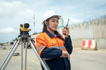 Portrait of Asian female survey engineer standing with surveyors equipment (theodolite) at road construction site.