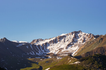 Large mountain range with steep slope and meadows at the foot