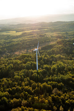 vue en hauteur d'une &eacute;olienne dans une for&ecirc;t avec des collines en arri&egrave;re plan lors d'un matin ensoleill&eacute;