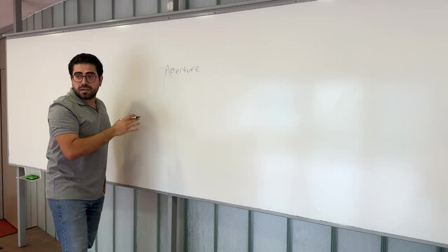 A male lecturer in his 30s lectures in front of a blackboard and in the classroom. The teacher stands alone and explains to the students and writes something on the blackboard.