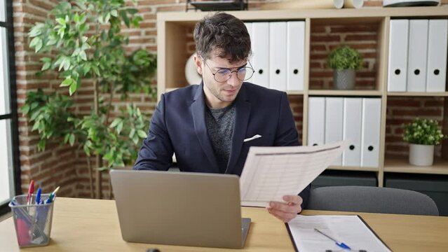 Young hispanic man business worker using laptop reading document at office
