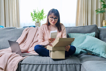 Mature woman sitting at home unpacking cardboard box with online shopping