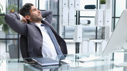 Cheerful young man holding hands behind head and keeping eyes closed while sitting at his working place