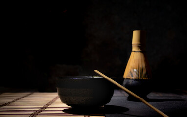 matcha tea black bowl with gray spots whisk and bamboo spoon on table with cane tablecloth with...