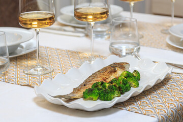 grilled seabass fish with a side dish of steamed broccoli served with a knife and fork with a glass of water and wine