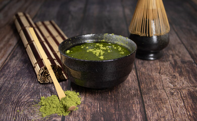 tea matcha black bowl with gray stains whisk and bamboo spoon on wooden table with tea green powder on top and a rolled cane tablecloth photo of diner close-up with space for text 