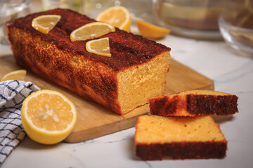 lemon cupcake with two pieces cut off on a beige table with a checkered towel and scattered lemons
