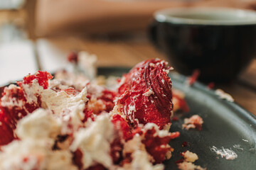 Messed up strawberry cake and cream on the dish with a cup of coffee.