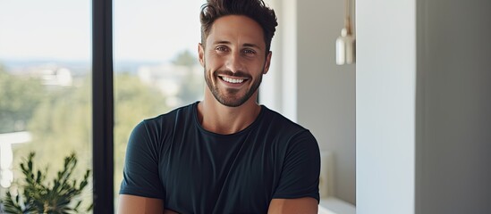Naklejka premium Portrait of a joyful young man holding tablet and smiling at camera by a window