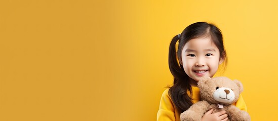 Cute Asian girl with teddy bear standing alone on yellow background
