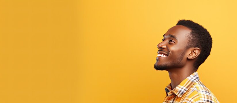 Happy African American man in checkered shirt standing alone looking away in front of yellow background