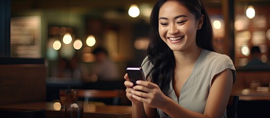 An Asian woman in a restaurant holding a smartphone with an empty screen ready for a message logo or advertisement