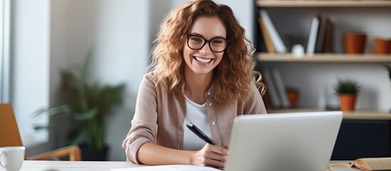 Smiling woman at desk using laptop and notebook studying online at home - obrazy, fototapety, plakaty