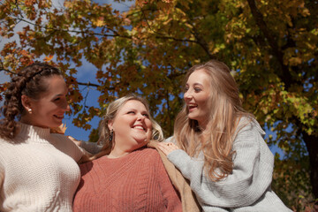 Fototapeta premium Multiracial female people with different bodies and hairs walking in the fall parks together. Friends wearing warm fashion clothes, knitted sweaters.