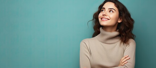 An attractive young woman full of joy confidence and optimism gazes upwards with her arms crossed - obrazy, fototapety, plakaty