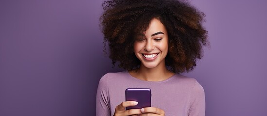 Woman with curly hair happily edits photo from dating app on mobile phone isolated on violet wall