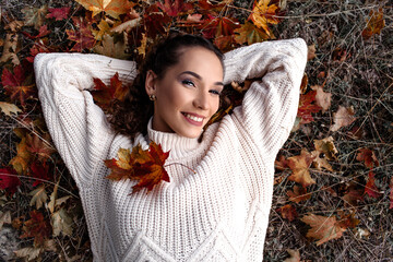 Portrait of a beautiful woman  hold the fall leaves and resting in the park. The happy girl wearing...