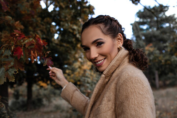 Portrait of a beautiful woman  hold the fall leaves and resting in the park. The happy girl wearing...