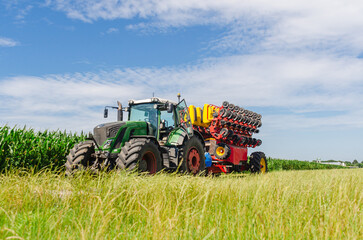 Seeder tractor in green corn field. Low angle view. Bright agricultural landscape with machinery.