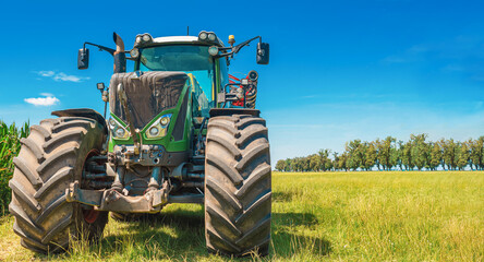 Large tractor on a summer field. Front view. Trees in the background. Agricultural landscape
