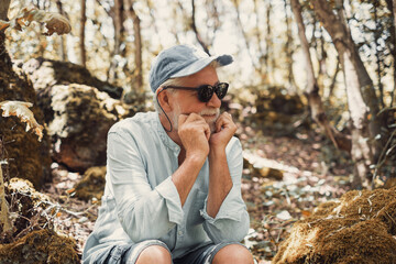 Portrait of pensive senior bearded man in black sunglasses sitting in park looking away