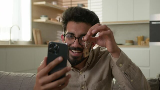 Happy Arabian business man Indian homeowner successful owner new rental house talk mobile phone video call in kitchen show bunch of keys rent realty mortgage buy apartment home relocation ownership