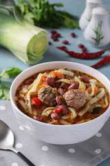Asian spicy soup with meatballs, beans and noodles on white bowl on blue background, Closeup