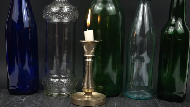 The flame of a burning candle in a brass candlestick is extinguished by a breath of wind. Burning white candle in old vintage brass and bronze candlestick against the background of glass multicolored 