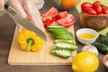 Chef cutting yellow pepper and different vegetables for salad close up. Hands in gloves with knife cooking vegetable, healthy vegetarian vegan diet food