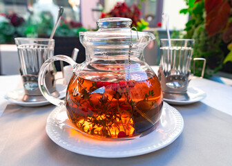 Glass teapot with herbal tea and cranberries and rays of light with faceted glasses in glass holders in the background. Delicious food close-up.