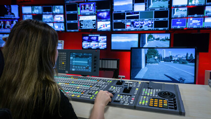 The director in the TV control room at the video mixer. Video switcher operator using the video mixer. Numerous screens in the TV control room. TV employee broadcasting live.