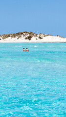 A couple walking on the turquoise blue waters of Formentera with a small mountain in the background