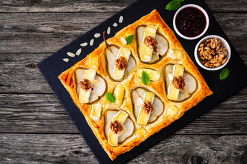 Baked puff pastry with pear and camembert cheese on baking paper on wooden table
