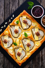 Baked puff pastry with pear and camembert cheese on baking paper on wooden table
