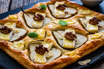 Baked puff pastry with pear and camembert cheese on baking paper on wooden table
