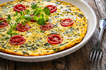 Omelette  - scrambled eggs with oregano, thyme, spinach and cherry tomatoes on wooden table
