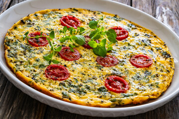 Omelette  - scrambled eggs with oregano, thyme, spinach and cherry tomatoes on wooden table
