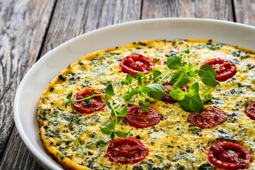 Omelette  - scrambled eggs with oregano, thyme, spinach and cherry tomatoes on wooden table
