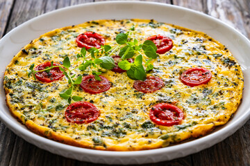 Omelette  - scrambled eggs with oregano, thyme, spinach and cherry tomatoes on wooden table
