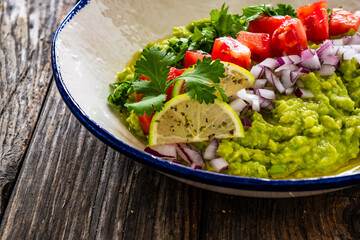 Guacamole with tomato, red onion and parsley on wooden table