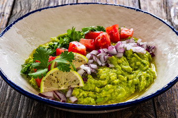 Guacamole with tomato, red onion and parsley on wooden table