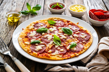 Upside down pizza with salami, mozzarella cheese and tomato sauce on wooden table