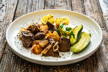 Fried liver with apples, potatoes and onion on wooden table
