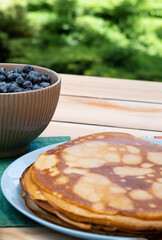 in the garden on the table there is a cup with fresh blueberries and a plate of blits © Катерина Толстая