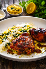 Greek style roasted chicken thighs with kritharaki rice and spinach on wooden table
