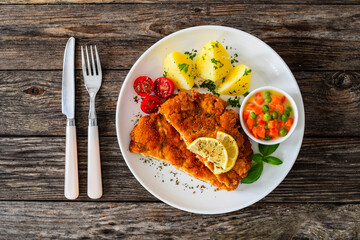 Crispy breaded seared chicken cutlet with boiled potatoes and vegetables on wooden table
 - obrazy, fototapety, plakaty