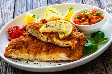 Crispy breaded seared chicken cutlet with boiled potatoes and vegetables on wooden table
